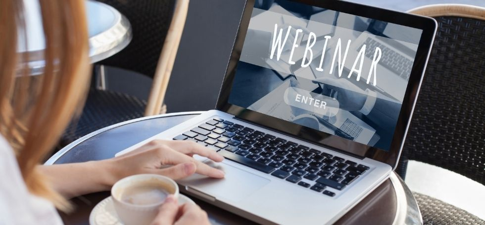 Woman on laptop with cup of coffee, screen says webinar