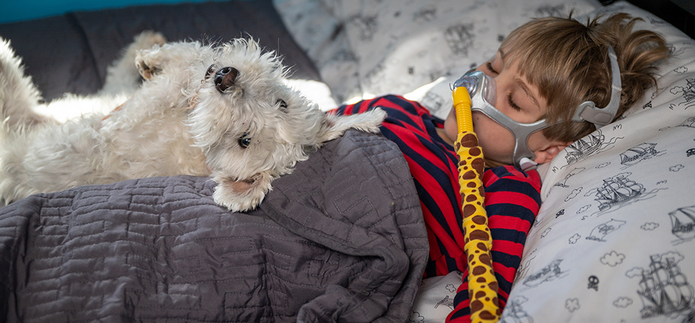 Child lying in bed with cpap and dog